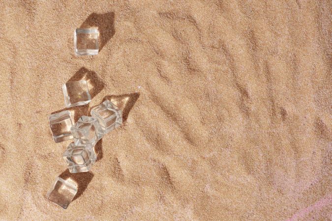 Flat lay of ice cubes on sand with shadow