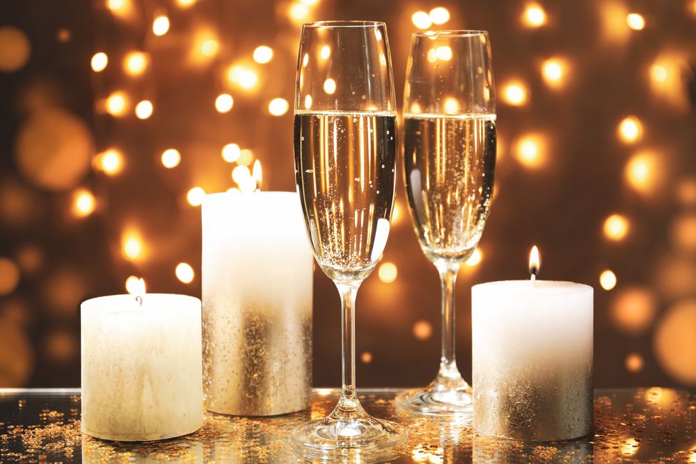 Champagne glasses and candles against blurred lights background, space for text