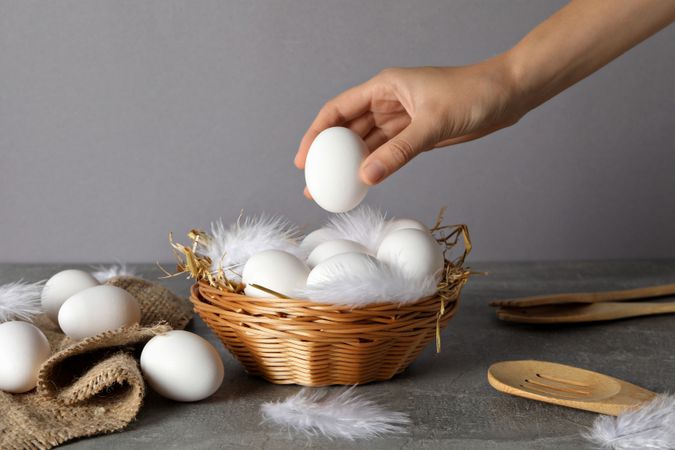 Eggs in a wicker basket, with a hand, on a gray background.