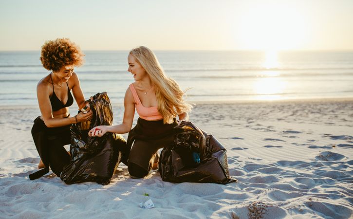 Two female volunteers in surf wet suits gathering garbage from the beach