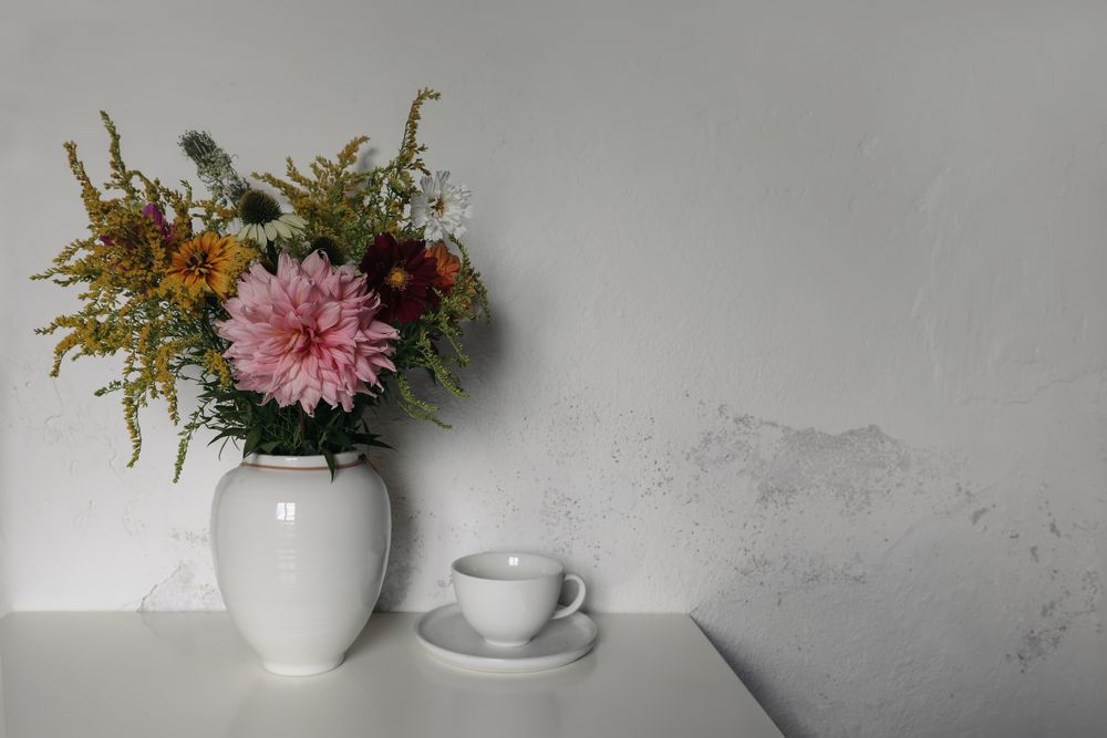 Beautiful bouquet of colorful dahlia, cosmos, solidago flowers next to cup and saucer