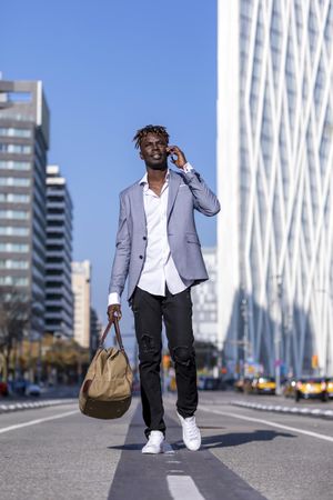 Black man wearing elegant suit standing in the street while talking on his phone out on a sunny day