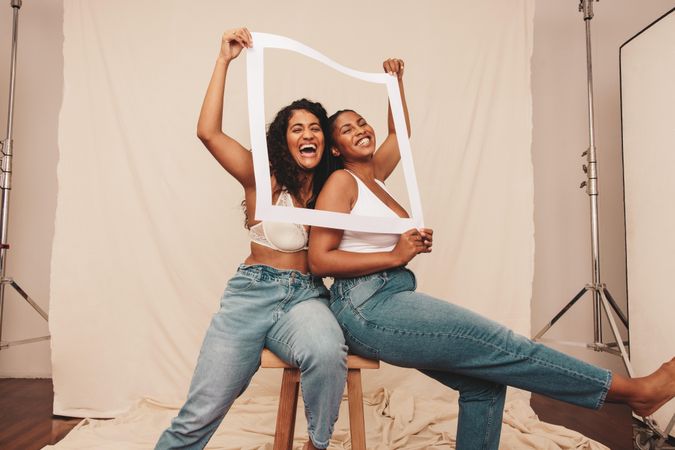 Best friends laughing through a white picture frame in studio