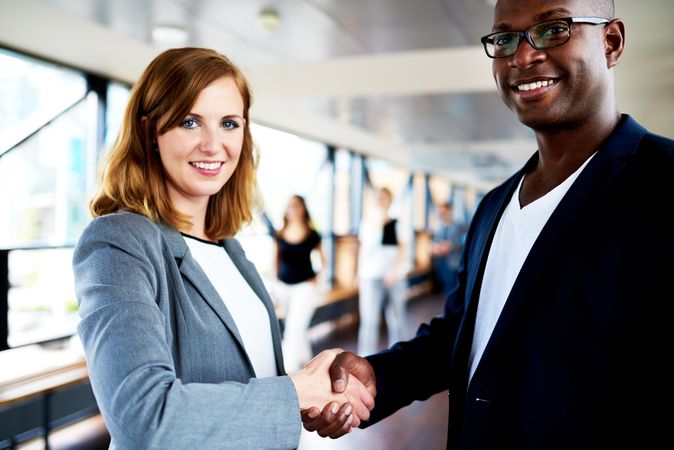 Black male and white female business associates shaking hands in hallway