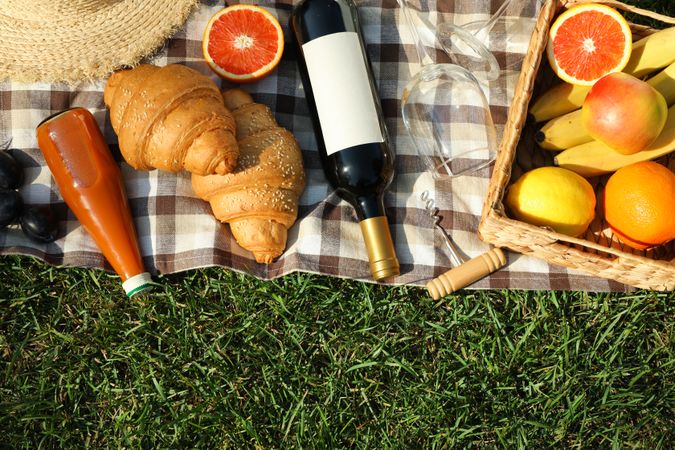 Composition with wine, croissants, fruits and towel on grass, top view