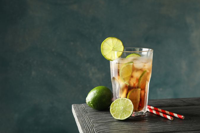 Glass of cold cola with citrus and ice on wooden table against dark background
