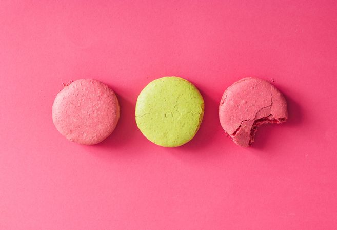French macaron in rows on bright, with bite on pink background