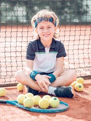 Content kid tennis player resting on court and smiling after mat