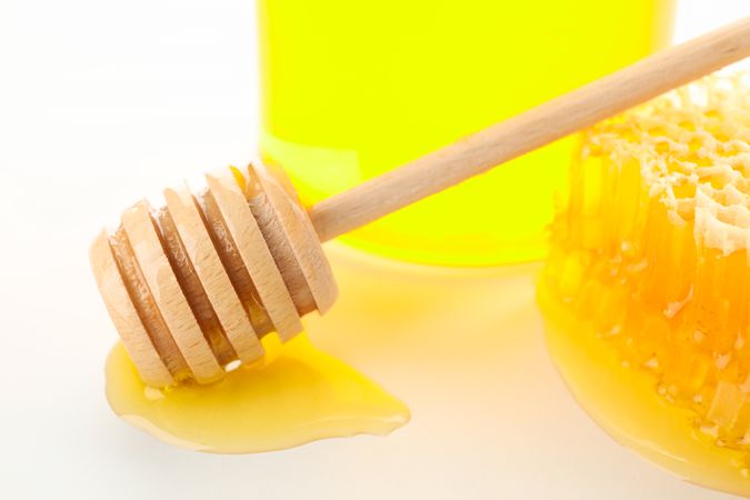 Glass jar, honeycomb and dipper on neutral background, close up