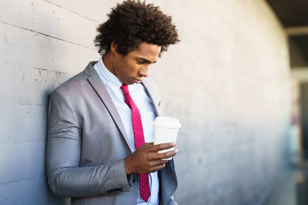 Man standing outside with his head down holding a coffee cup