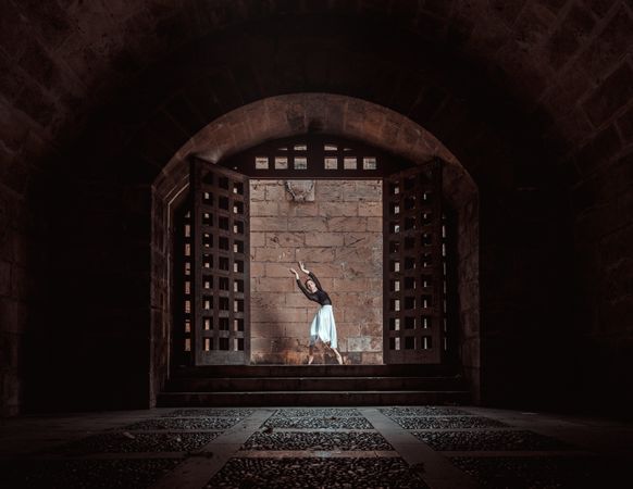 Graceful ballerina dancing in dark passage near stone brick