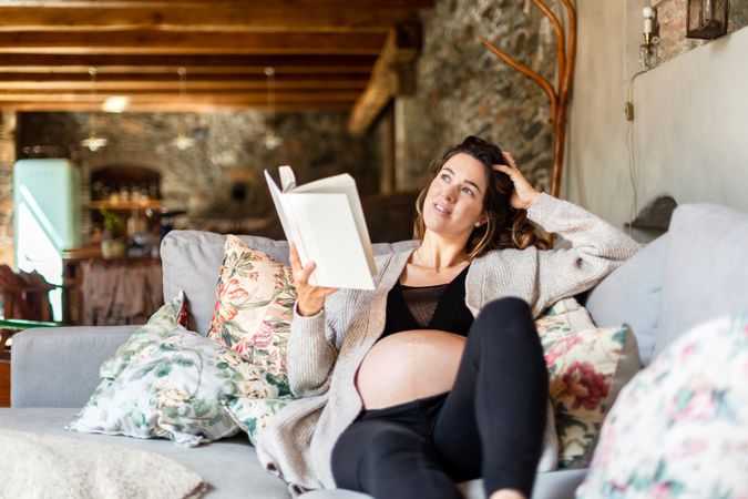 Calm pregnant woman enjoying reading a book on her home sofa