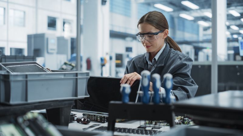 Female Worker Disassembling Old Laptops To Recycle Electronic Components For Sustainable Production At an Electronics Factory.