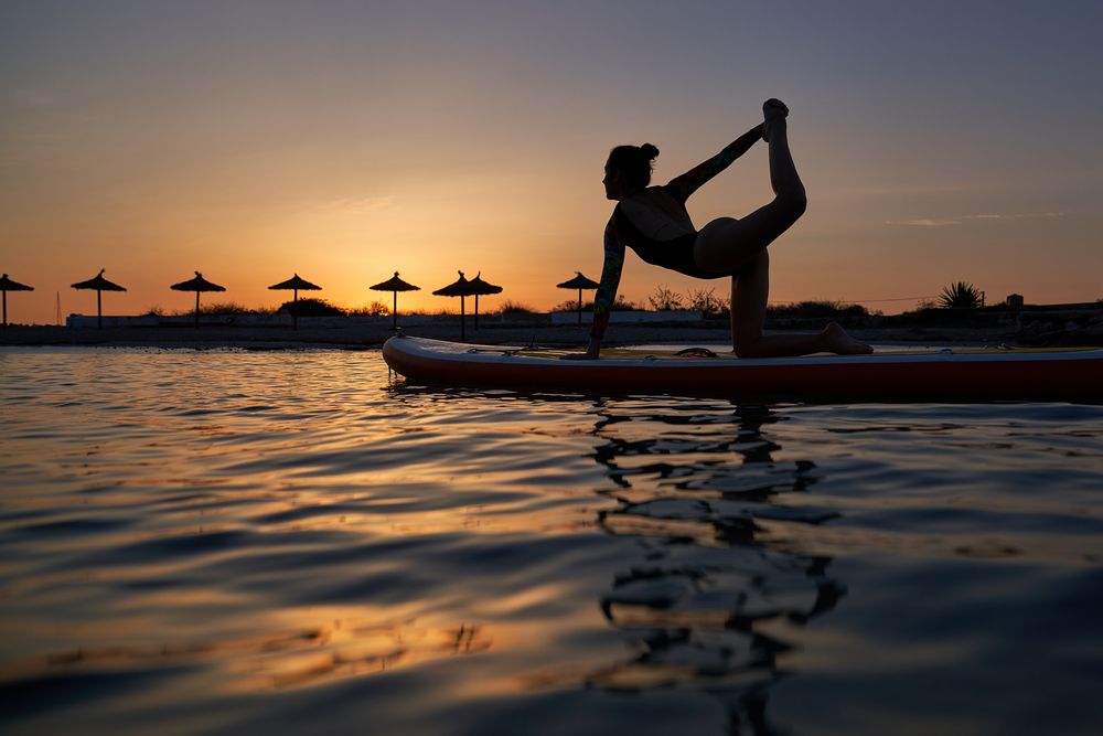 Silhouette of young woman taking Tiger pose on SUP board