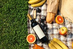Bottle of wine, baguette, fruits, straw hat and towel on grass, space for text