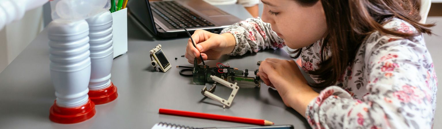 Female student connecting wire on electrical circuit in robotics class