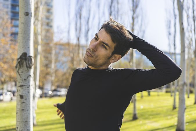 Sporty man stretching neck and head after jogging in city public park