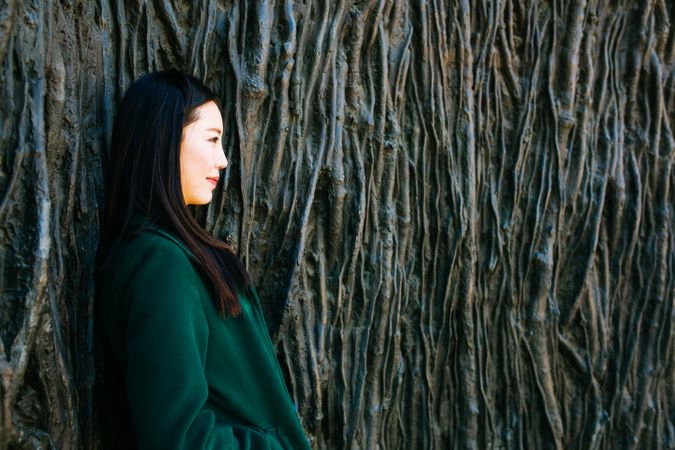 Pensive Asian woman leaning on rough wall