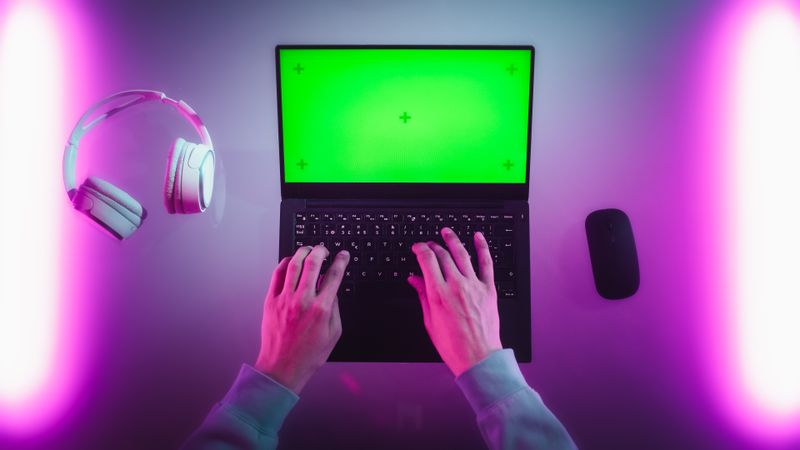 Anonymous Designer Typing on a Laptop with Mock Up Green Screen Chromakey Display. Software Developer or Gamer Using a Computer, Working on a Creative Project, Chatting with Team. Top Down View