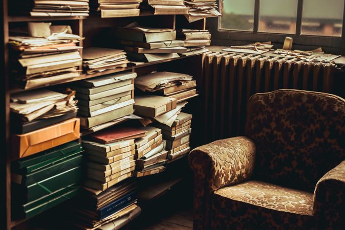 Old armchair near shelves with heap of papers