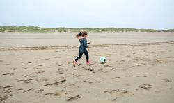 Little girl playing soccer on the beach