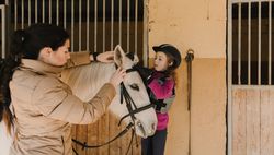 Woman and girl putting bridle on horse