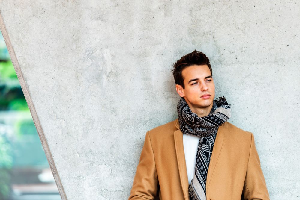 Young man wearing winter coat and scarf looking away against cement pillar