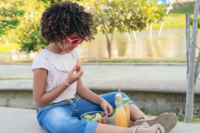 girl eating vegetables while sitting in the park in summertime