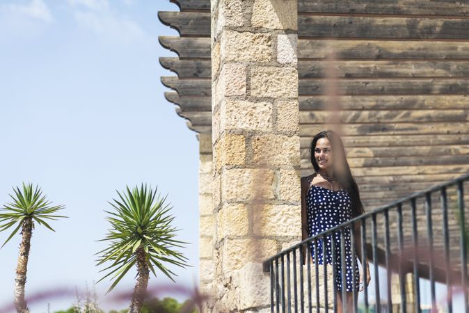 Smiling woman in blue dress leaning on wall while looking away