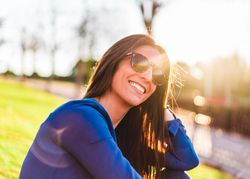 portrait of young woman with sunglasses sitting on grass in park