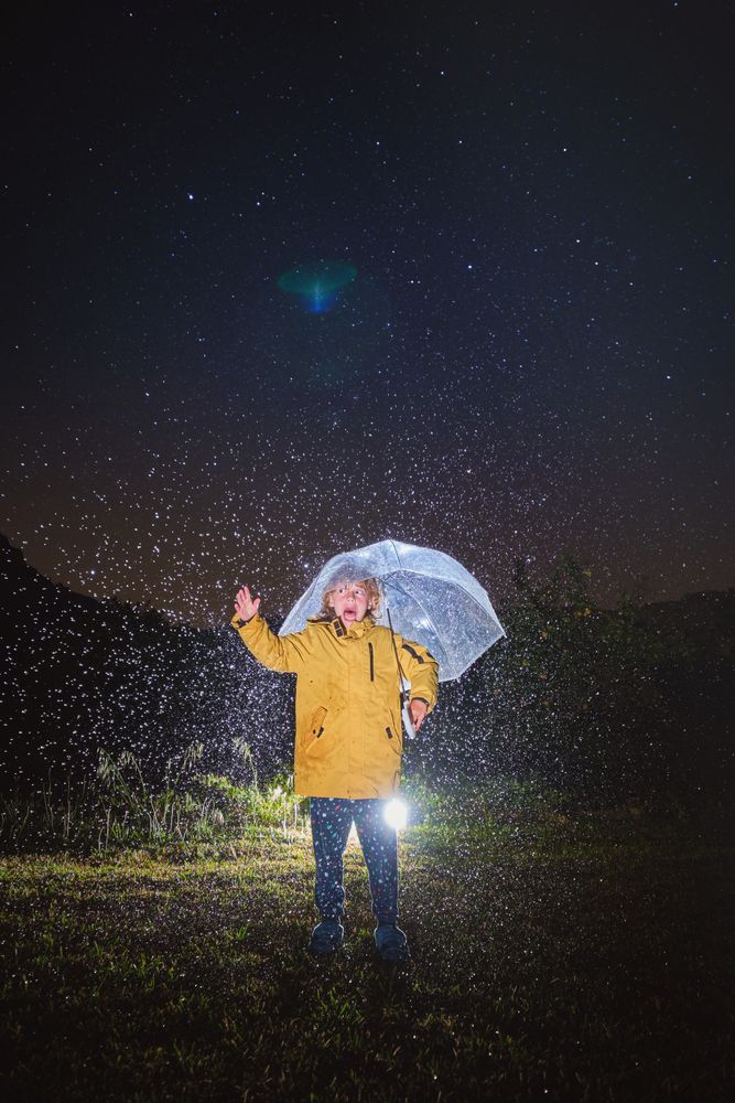 Unrecognizable kid in bright raincoat under umbrella during rain