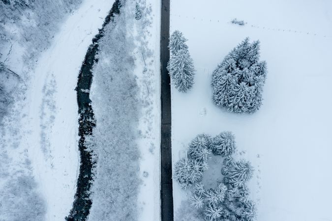 Winter road near mountain river in snowy scenery, drone aerial view