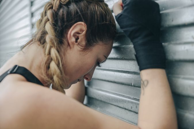 Tired sportswoman resting on a metal wall