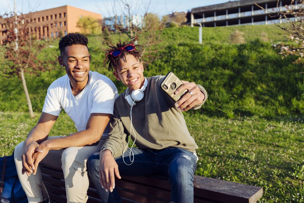 Young Black men sitting on bench with smartphone