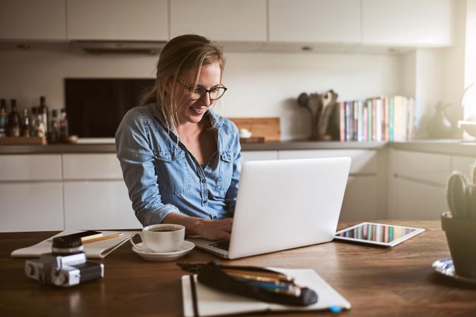 Woman smiling at laptop in her kitchen