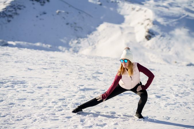 Stylish woman doing yoga exercise on snowy terrain