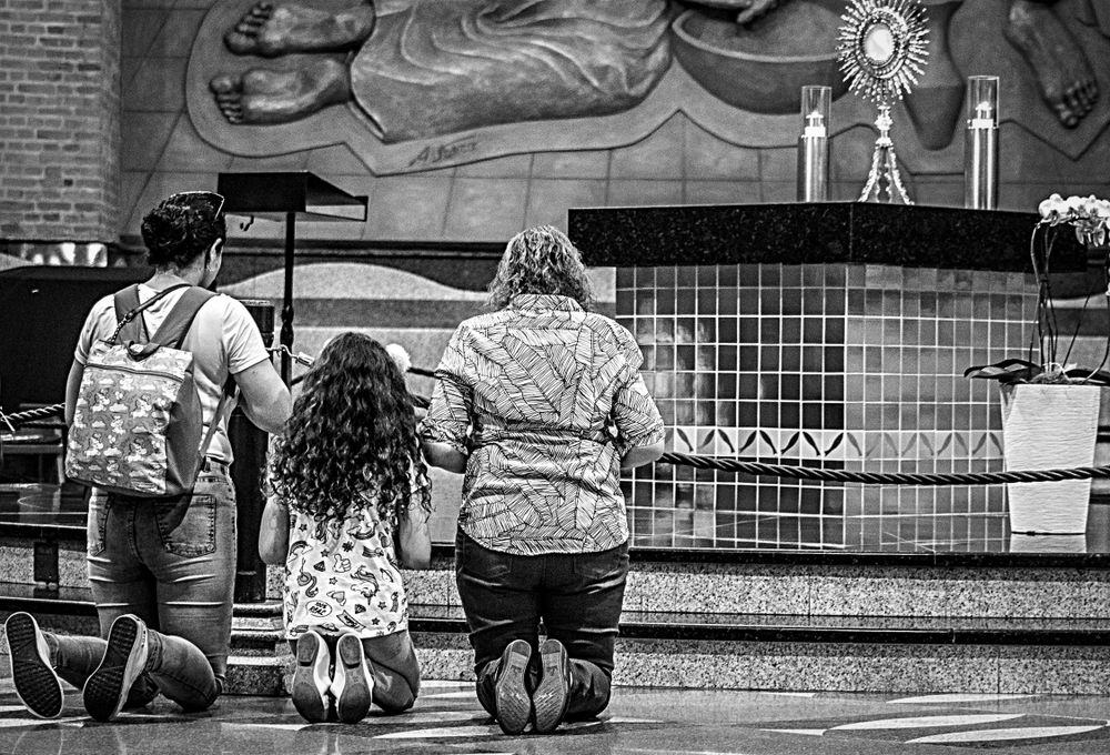 Grayscale photo of woman and man and girl praying at the alter