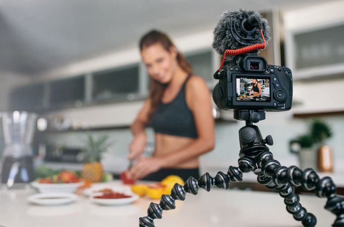 Woman slicing fruit on kitchen table facing digital camera