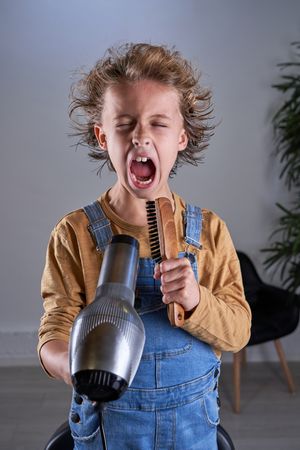 Child in a hairdresser's singing with a hairdryer and a brush