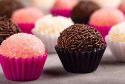 Close up of rows of, strawberry, coconut & chocolate flavored truffles on marble table