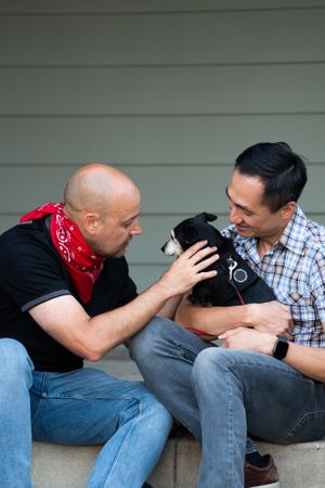Two male partners sharing affection with their dog on their front porch