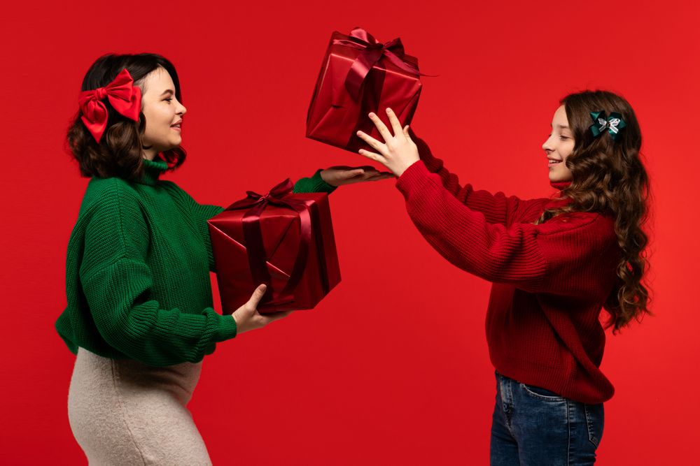 Woman and girl juggle large red boxes in holiday studio