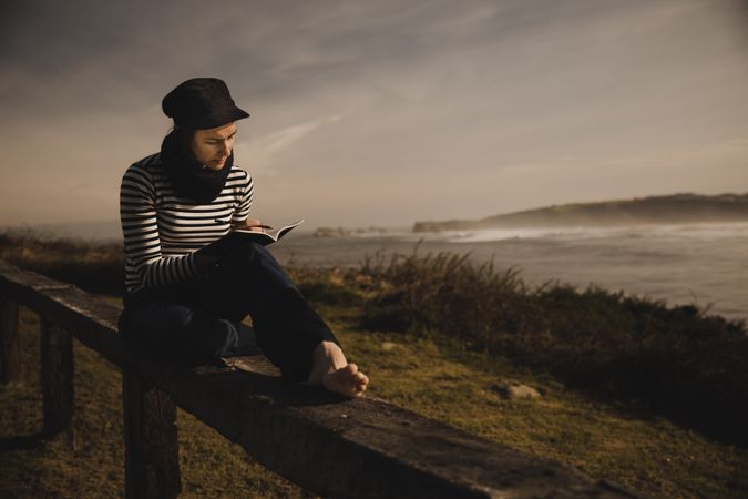 Woman writing in notebook and sitting on bench on shore near water