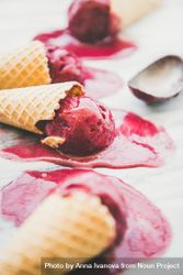 Cones of dark berry ice cream melting on marble slab, vertical composition, side view with scoop 56N9V5