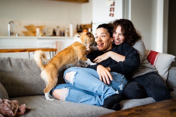 Happy female couple holding each other in living room with dog