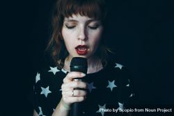 Woman in star print shirt holding microphone singing against dark background 41OAg0
