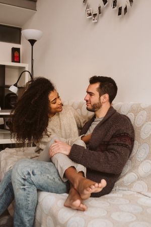 Young multiracial couple hugging on sofa