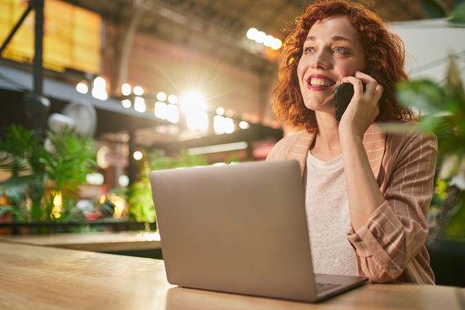 Young woman talking on phone while working on laptop