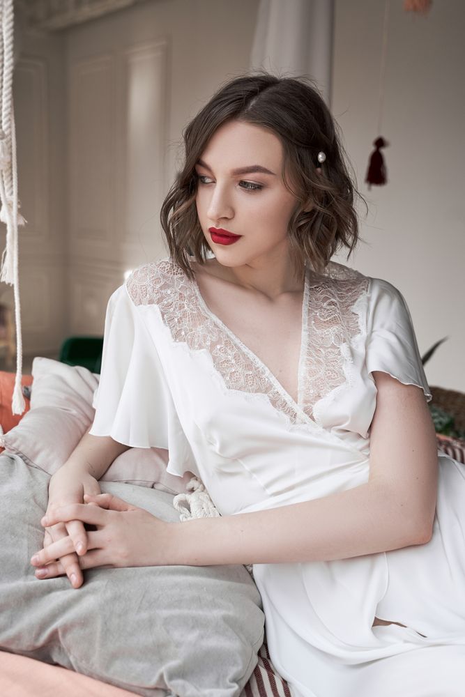 woman with red lips in white dress looking at camera while sitting on floor beside sofa