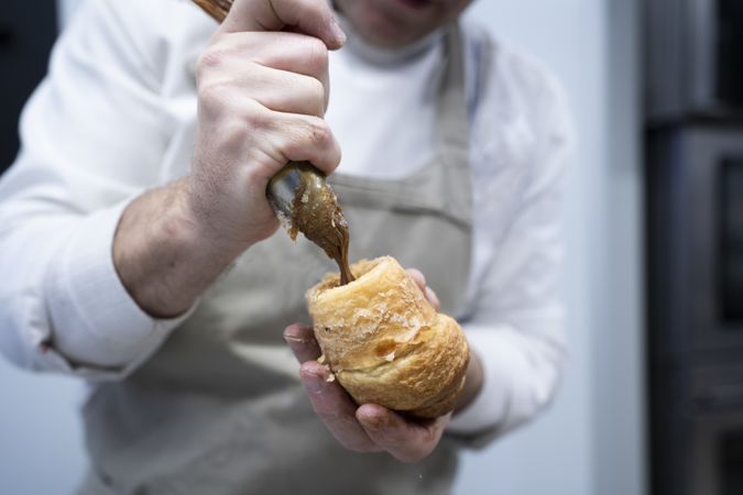 Confectioner pouring chocolate filling into croissant